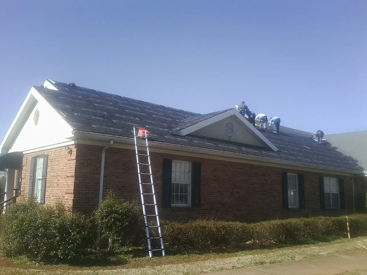 Crew tearing shingles off a brick ranch roof with a ladder set — Emergency Roof Repair work by our crew in Hazel Green
