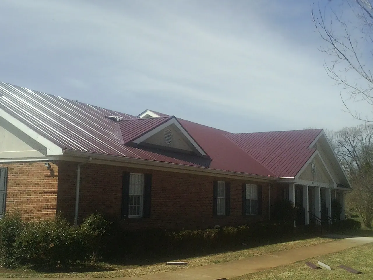 Red metal roof with gabled entries on a long brick building, from a Hail Damage Roof Repair job in Hazel Green