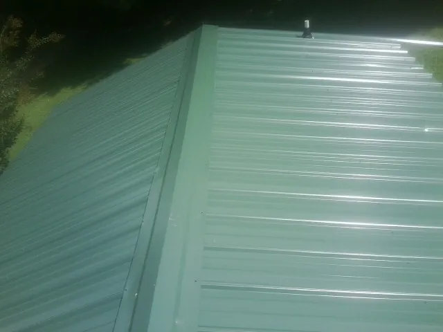 New green metal panels meeting at the ridge of a roof — Flat Roof Repair work by our crew in Hazel Green