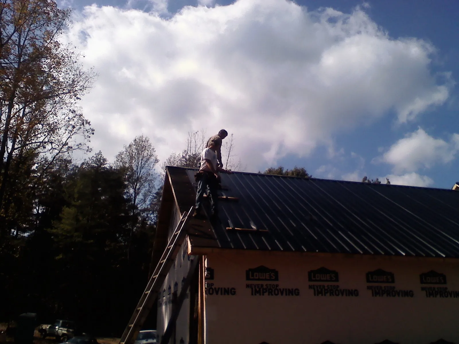 Roofer fastening dark metal panels high against a cloudy sky, from a Roof Inspection job in Hazel Green