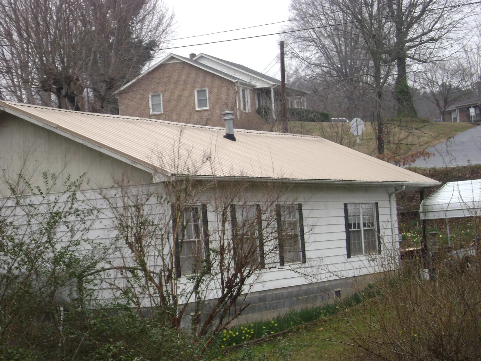 Tan metal roof on a white sided house set into a hillside — Commercial Roofing by Roofing Brothers in Hazel Green