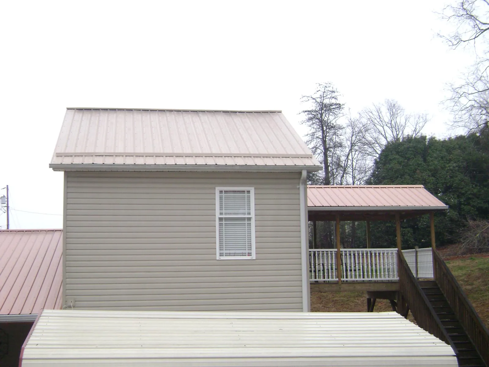 Tan metal roofs on a two story addition and attached porch, from a Roof Replacement job in Hazel Green